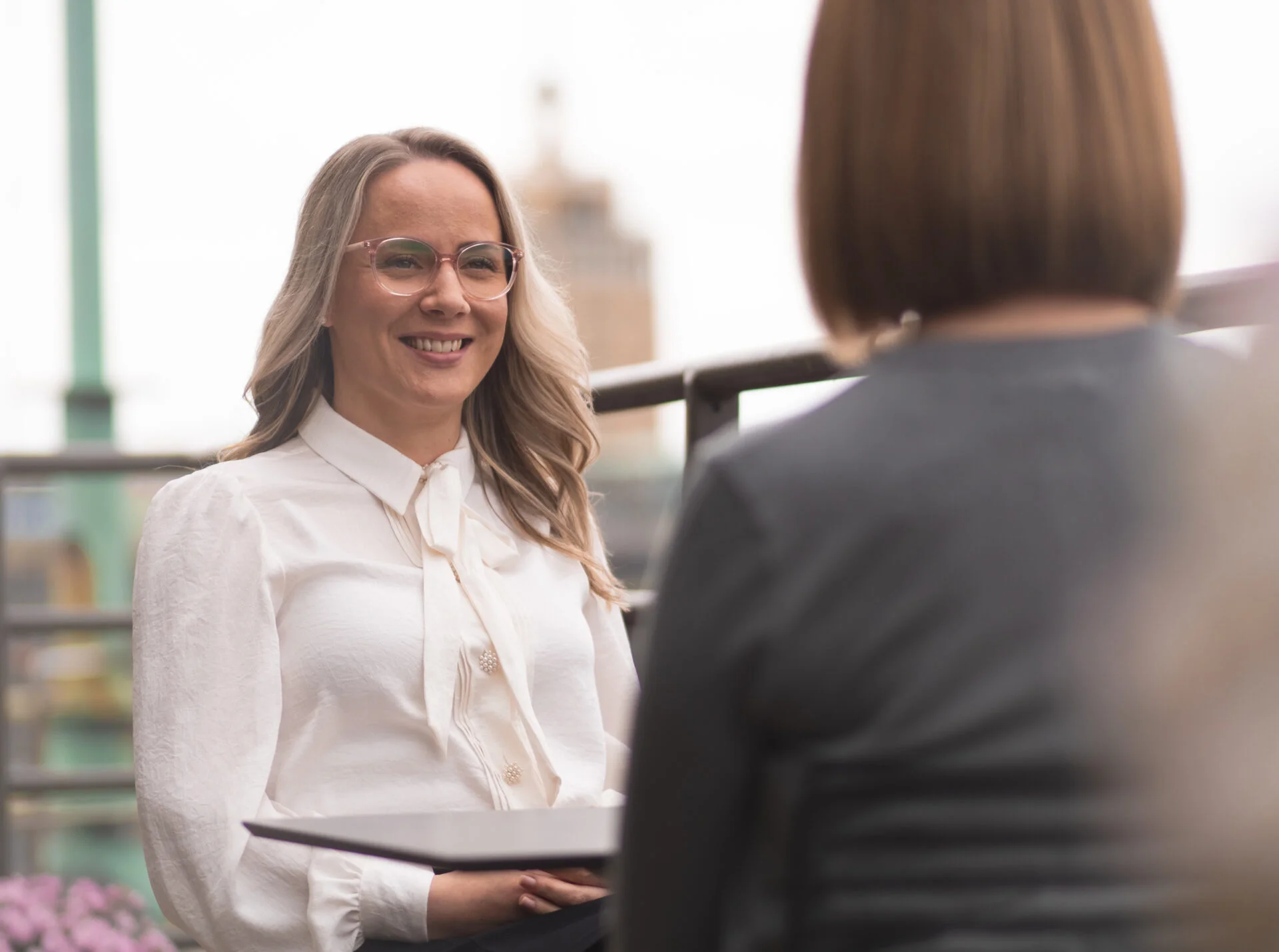 Woman with glasses smiling on a balcony with a colleague