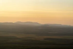 Scenic view of rolling hills under a golden sunset, with vast forested plains in the foreground."